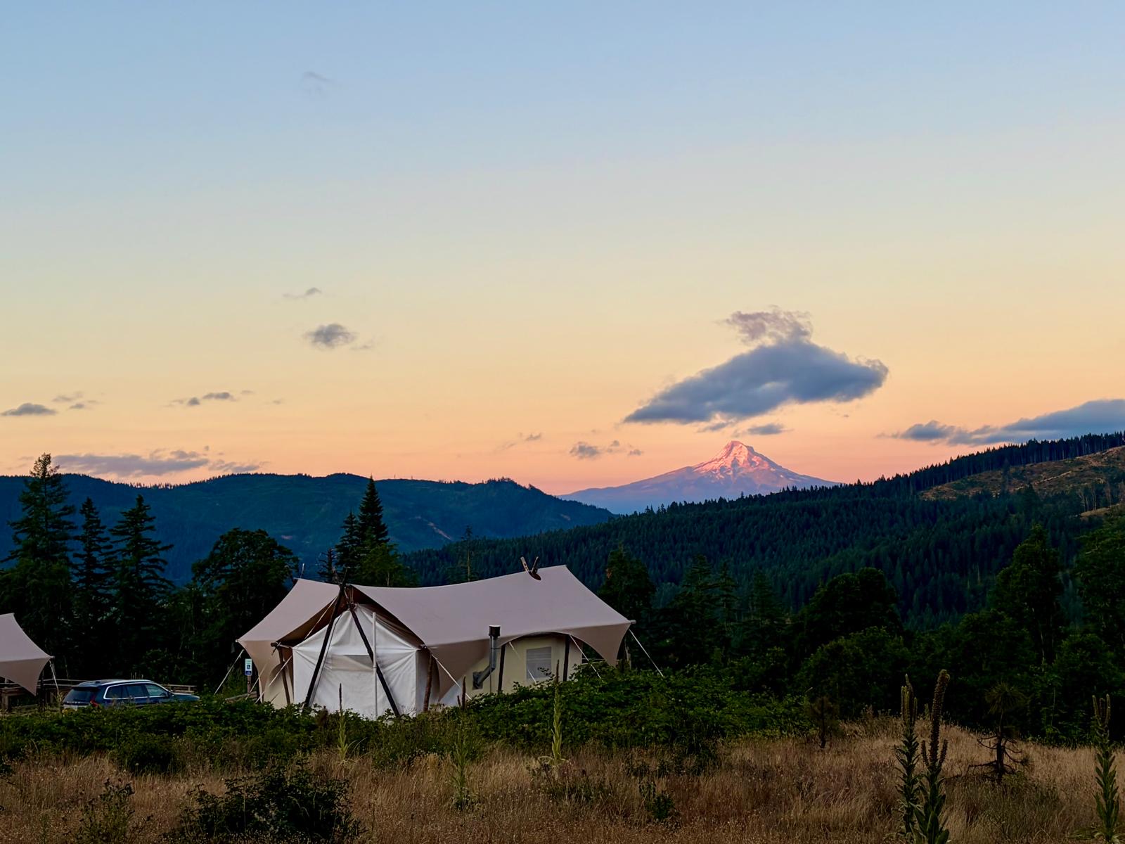 Glamping tents at dusk beneath a mountain peak