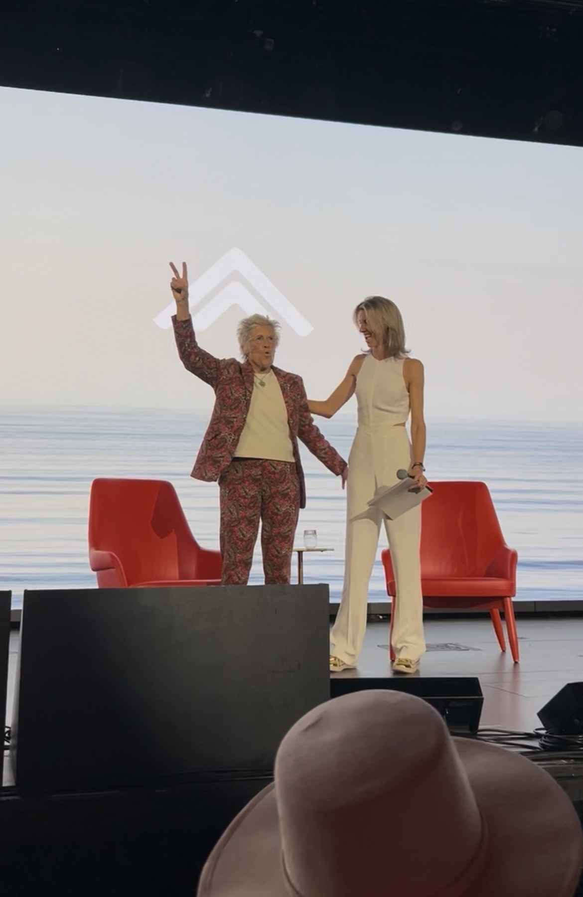 Speakers on stage, ocean horizon projected behind